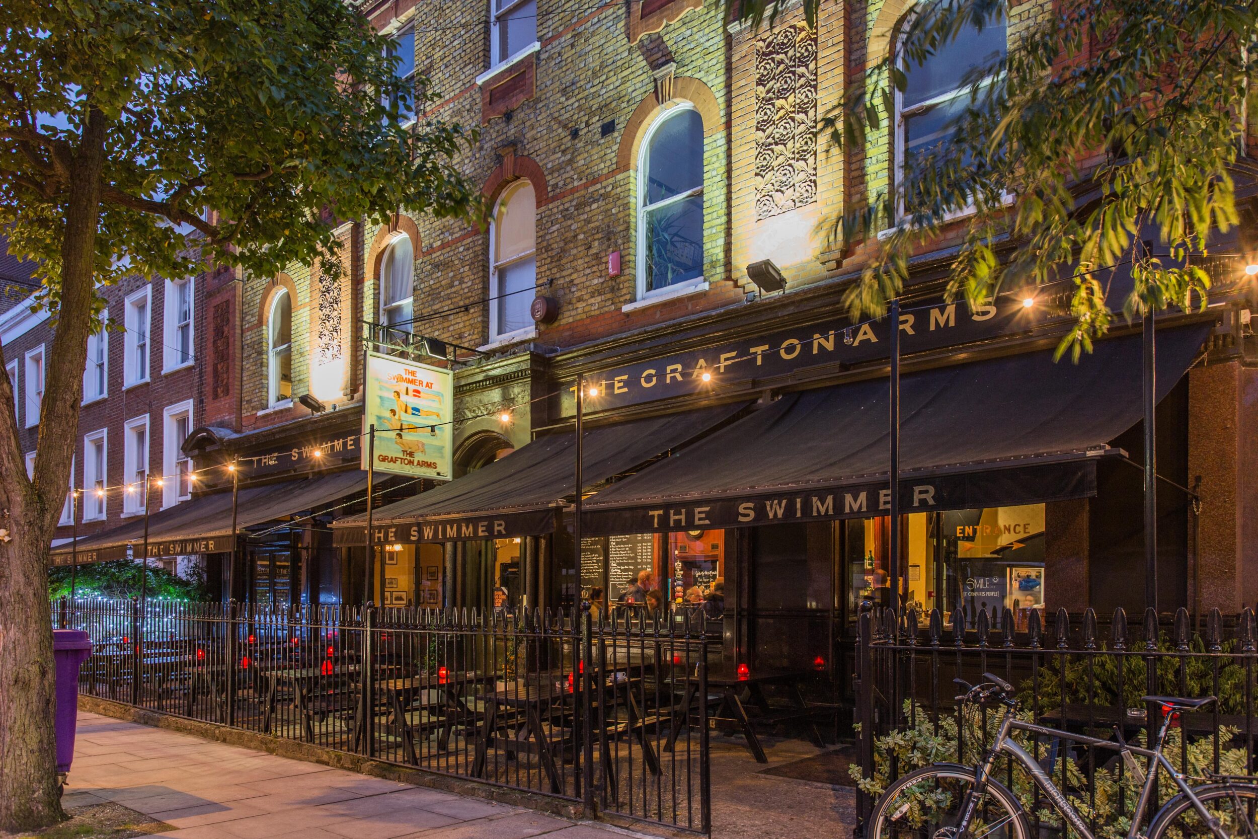 A photograph of the exterior of a pub owned by Remarkable Pubs- beautiful soft lighting, and outside seating. Graphic design produced by Barefaced Studios, design agency based in Islington, North London.